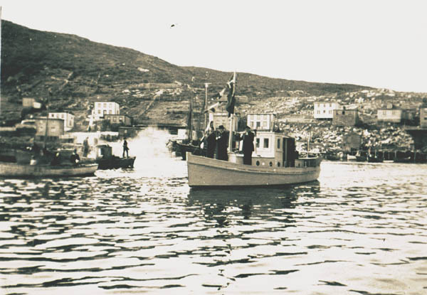 306: "This is Bishop Skinner, Rev. Doctor O'Keefe and Father Fyme in Vick Mulrooney's boat leaving  here to go to Merasheen. All the boats here accompanied them out". Red Island harbour. [courtesy of Anita (Delurey) Corcoran]